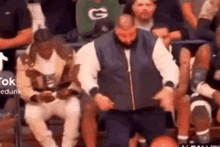 a group of people are sitting in a stadium watching a basketball game and a man is kneeling down .