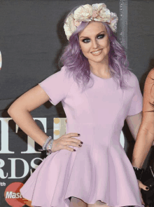 a woman with purple hair and a floral headband stands in front of a mastercard sign