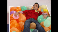 a man in a red shirt is laying in a box full of balloons