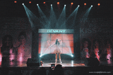 a woman singing on a stage in front of a devant sign