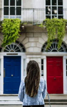 a woman is standing in front of a building with two doors one blue and one red