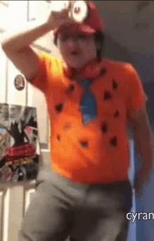 a man in an orange shirt and a red hat is dancing .