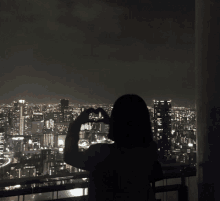 a woman is making a heart shape with her hands in front of a city skyline