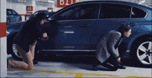 a man and a woman kneeling next to a car in a parking garage with a sign that says b11