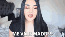 a woman with long black hair is sitting on a bed with her eyes closed and says me vale madres