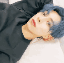 a young man with blue hair is laying on a bed with his head on a pillow .