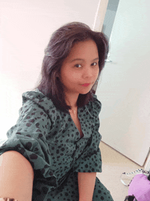 a woman wearing a green dress with black polka dots is taking a selfie