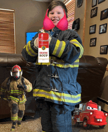 a young boy dressed as a fireman holds a container of creative soup