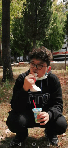 a boy wearing a sweatshirt that says ito is drinking from a cup