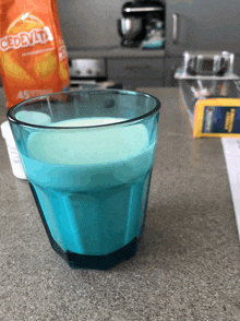 a glass of blue liquid next to a bag of cedevita chips