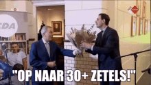 a man in a suit is holding a bouquet of flowers while another man says " op naar 30 + zetels "