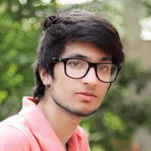 a young man with glasses and a pink shirt is looking at the camera .