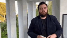 a man with a beard in a suit is standing on a porch holding a cell phone .