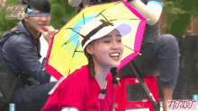 a woman wearing a red shirt and a rainbow colored umbrella smiles in front of a tv screen that says htv online