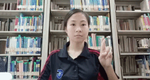 a woman wearing a shirt with the letter d on it stands in front of a library full of books