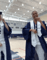 two female graduates are dancing in front of a gym with a banner that says ' athletics ' on it