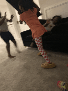 a little girl wearing a pink shirt and hearts on her pants is standing in front of a couch