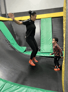 a woman is jumping on a trampoline with a child watching