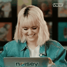 a woman in a denim jacket is smiling while looking at a laptop that says noisey on it