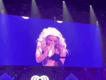 a woman singing into a microphone on a stage at iheart radio