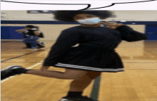 a girl wearing a mask stands on one leg on a gym floor