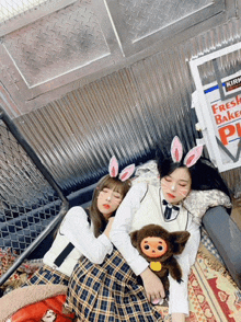 two girls laying next to each other with bunny ears on their faces in front of a kirkland fresh bakery sign