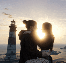 a couple standing in front of a lighthouse with the sun shining through them