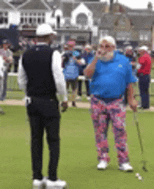 a man in a blue shirt and pink pants is standing on a golf course with a golf club .