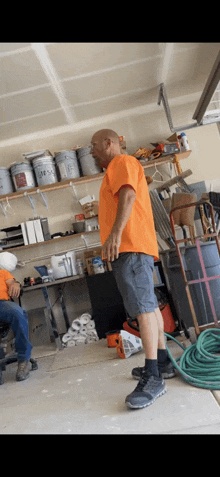 a man in an orange shirt is standing in a garage with other men