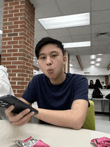 a young man is sitting at a table looking at his cell phone