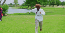 a man in a white shirt and tie is standing in a grassy field next to a body of water .