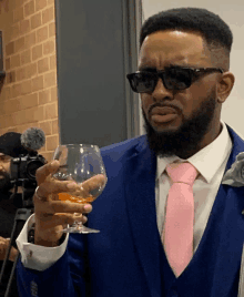 a man in a blue suit and pink tie holds a glass of wine