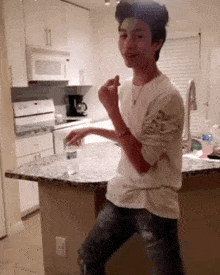 a young man in a white shirt is standing in a kitchen with a bottle of water on the counter