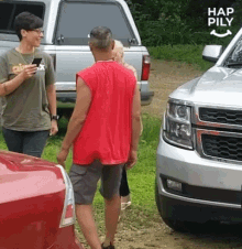 a man in a red shirt is standing next to a silver truck and talking to a woman in a green shirt .