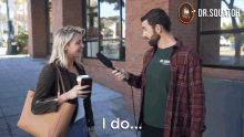 a man holding a microphone talking to a woman who is holding a cup of coffee and says i do