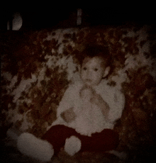 a baby is sitting on a couch with a floral blanket