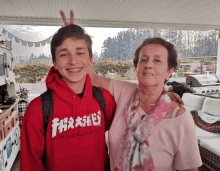 a young boy wearing a red thrasher hoodie stands next to an older woman