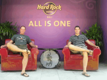 two men sit in red chairs in front of a sign that says hard rock hotel bali