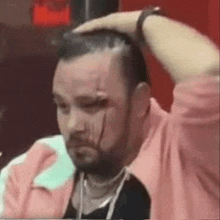 a man with a beard and a bandage on his face is sitting at a table with his hand on his head .