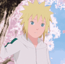 a young boy with blonde hair and blue eyes stands in front of a tree with pink flowers