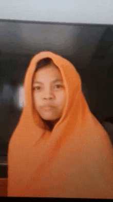 a young girl wearing an orange hijab is sitting in front of a tv .