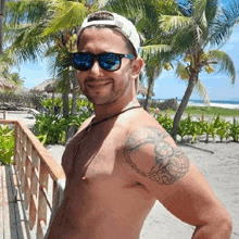 a shirtless man with a tattoo on his shoulder is standing on a beach .