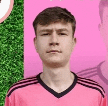 a young man wearing a pink adidas shirt stands in front of a pink background .