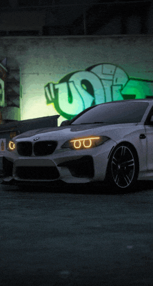 a white bmw is parked in front of a wall with graffiti on it that says usr