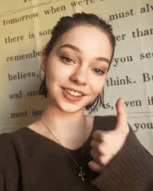 a young woman is smiling and giving a thumbs up in front of a quote .