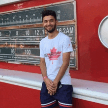 a man wearing a white t-shirt with a maple leaf on it is standing in front of a radio station .