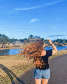 a woman standing on a road with her hair blowing in the wind in front of a lake