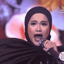 a woman in a hijab singing into a microphone with the word lange on the bottom right