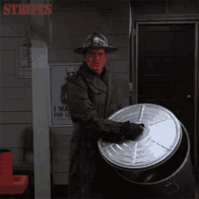 a man in a hard hat is holding a large metal barrel in front of a sign that says stripes