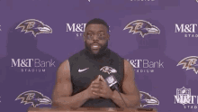 a man stands at a podium with a microphone in front of a purple wall that says m & t bank stadium